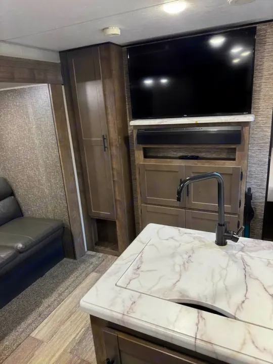 Explore this modern RV rental interior featuring a compact kitchen with a marbled countertop, sink, TV, and sofa. Ready for adventure.. KZ Connect SE 2021