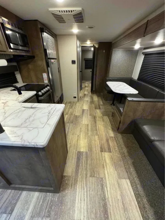 This RV rental interior features a modern kitchen with microwave, fridge, and marble-look counters, a dining booth, and wood-style flooring.. KZ Connect SE 2021
