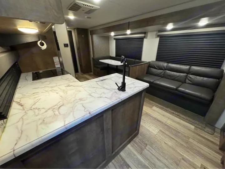 Modern RV rental interior: kitchen with marble-look counters, a black sofa, and dining booth. Ideal for comfortable travel.. KZ Connect SE 2021