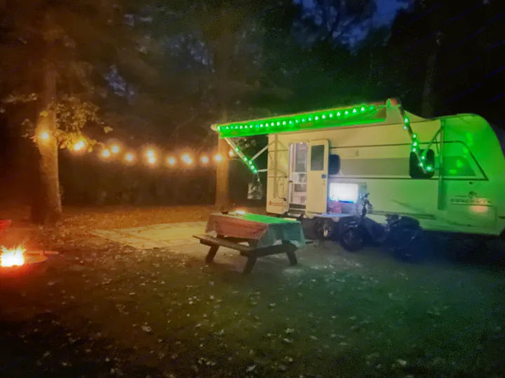 Vibrant rv rental camping scene at night with bright green lights, string lights, and a blazing campfire.. Coachmen Freedom Express 19SE 2025