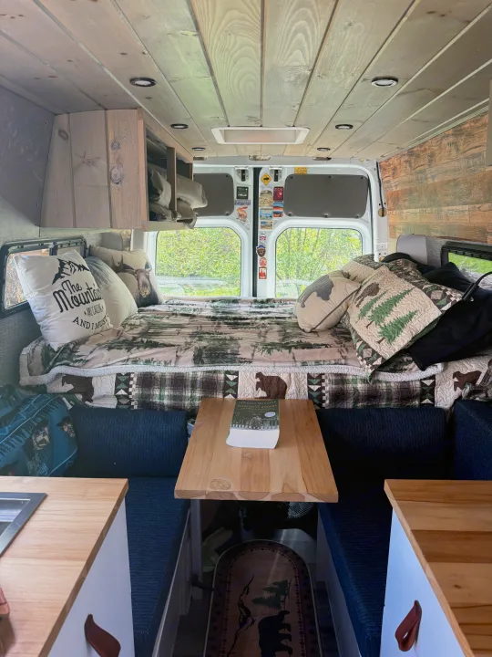 Cozy RV rental camper van interior: nature-themed bed, wooden ceiling/walls, kitchen, and dining nook for comfortable travel.. Mercedes Sprinter 2011
