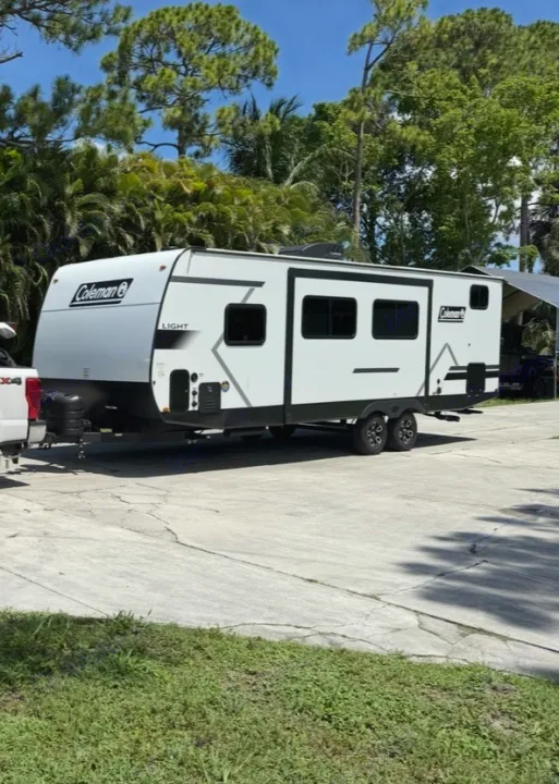 Coleman Light RV rental, a white travel trailer, parked with a truck on concrete, lush trees in background. Ready for adventure.. Keystone RV Coleman Light 2025