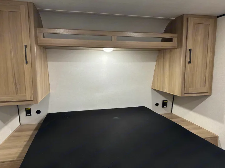 RV rental's cozy bedroom. Features a bed, light wood overhead cabinets, and convenient side charging ports. Bright & functional space.. Keystone RV Coleman Light 2025