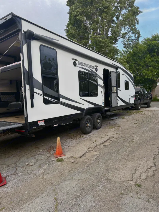 Genesis rv rental toy hauler with its rear ramp down, showcasing a spacious interior, parked alongside a black pickup truck.. Genesis Supreme Rv Genesis Supreme 2019