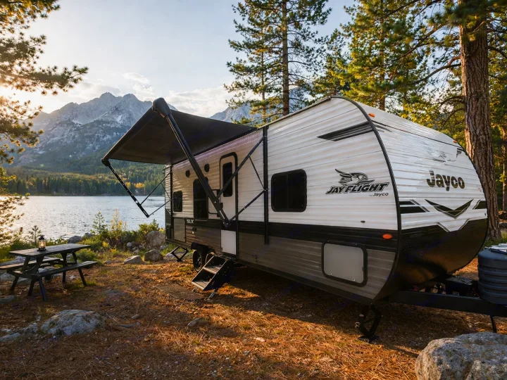 Enjoy nature with this Jayco travel trailer rv rental. Parked lakeside with mountains, trees, & a picnic table.. Jayco Jay Flight SLX 2024