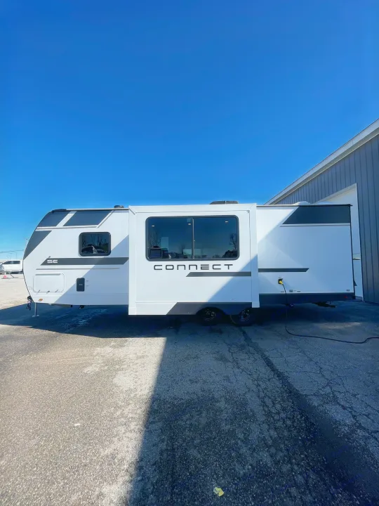 White "CONNECT" travel trailer RV rental with an extended slide-out, parked on asphalt under a clear blue sky.. KZ Connect 241BHKSE 2026