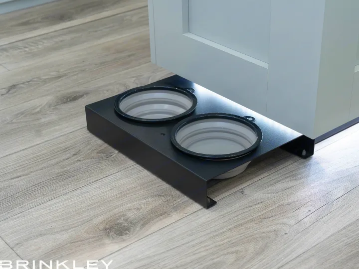 Pet-friendly RV rental convenience: collapsible pet bowls in a sleek stand, tucked under a cabinet, on laminate flooring.. Brinkley Air 295 2025