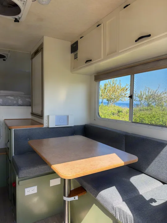 Bright RV rental dinette with a scenic window view of the ocean & trees. Features a table & gray bench seating.. Chevrolet Silverado 2500HD 2008
