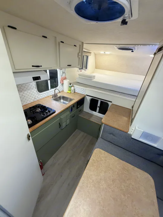 Bright rv rental interior: renovated kitchen with stove & sink, cozy bed, and dinette. Efficient compact living space.. Chevrolet Silverado 2500HD 2008