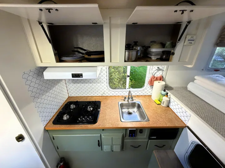 Inside an RV rental: a compact galley kitchen featuring a stovetop, sink, storage, and a stylish scalloped backsplash.. Chevrolet Silverado 2500HD 2008