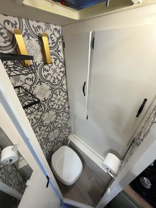 Compact RV rental bathroom with modern patterned wallpaper, white cabinets, toilet, and clever storage solutions.. Chevrolet Silverado 2500HD 2008