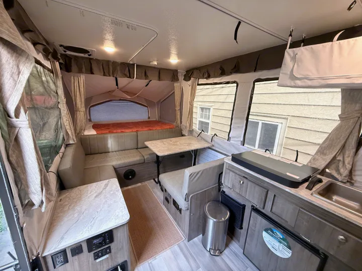 Interior of a compact pop-up RV rental, featuring a dinette, bed, and small kitchen for comfortable camping.. Forest River Rockwood ESP 2022