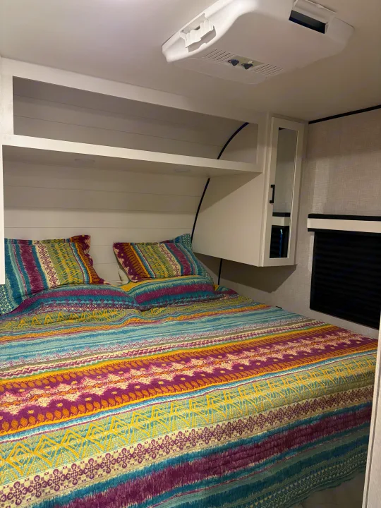 Cozy RV rental bedroom with colorful patterned bedding, overhead storage, and AC unit for a comfortable stay.. Jayco Jay Flight SLX 2025