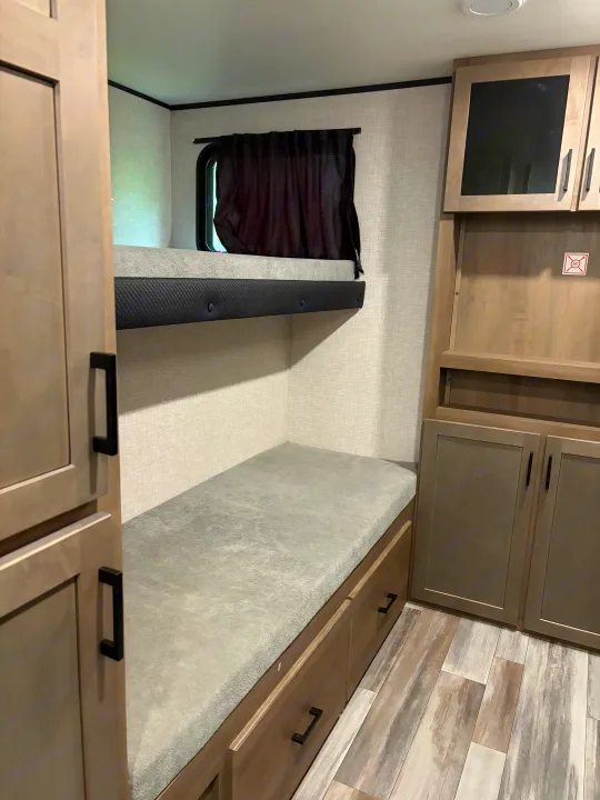 RV rental interior features cozy bunk beds with storage, light-toned cabinets, textured walls, and wood-look flooring.. Jayco Jay Flight SLX 2025