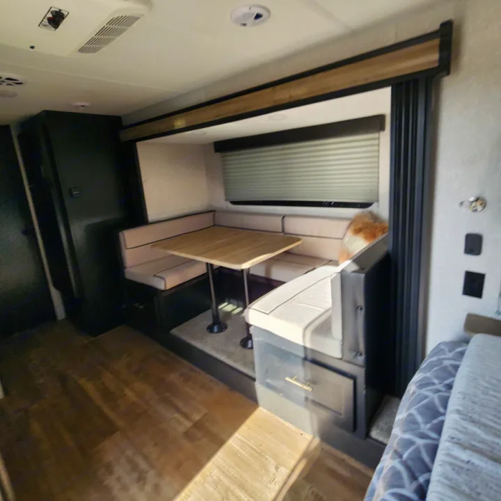 RV rental interior: cozy dinette with light bench seats, a wooden table, dark cabinetry, and wood-patterned floor.. Forest River Cherokee Wolf Pup Black Label 2022