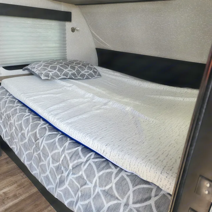 Cozy rv rental interior with a bed made up with gray patterned bedding, a white textured mattress topper, and window blinds.. Forest River Cherokee Wolf Pup Black Label 2022