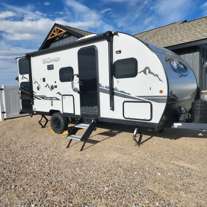 Modern white Wolf Pup rv rental on gravel. Steps down, stabilizers set, and ready for your outdoor adventure.. Forest River Cherokee Wolf Pup Black Label 2022