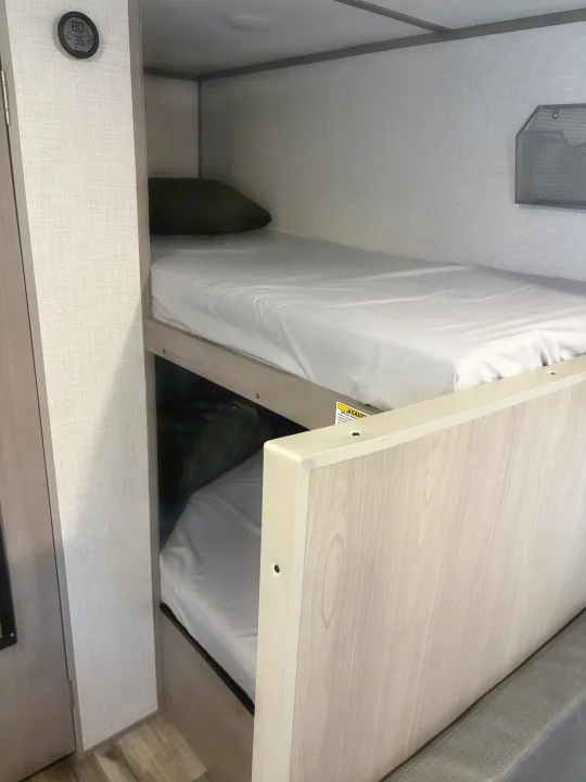 RV rental bunk beds feature light wood, white bedding, a digital thermometer (80°F), and mesh wall storage.. Dutchmen Coleman Lantern LT 2022