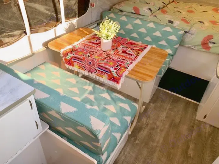 Cozy rv rental interior: bright dining area with teal patterned cushions, wooden table, colorful throw, and a comfy bed.. Viking Pop Up 2004