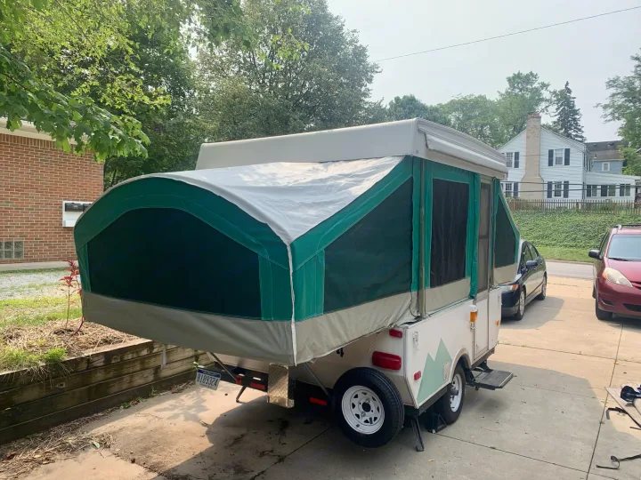A green and white pop-up camper, a type of RV, is fully extended in a sunny driveway. Consider for rv rental.. Viking Pop Up 2004