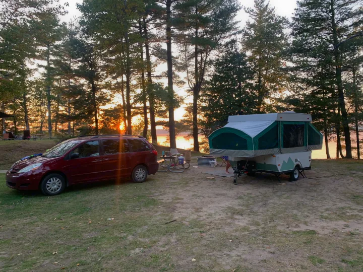 Golden sunset at a lakeside campsite with a red minivan and a pop-up RV rental.. Viking Pop Up 2004