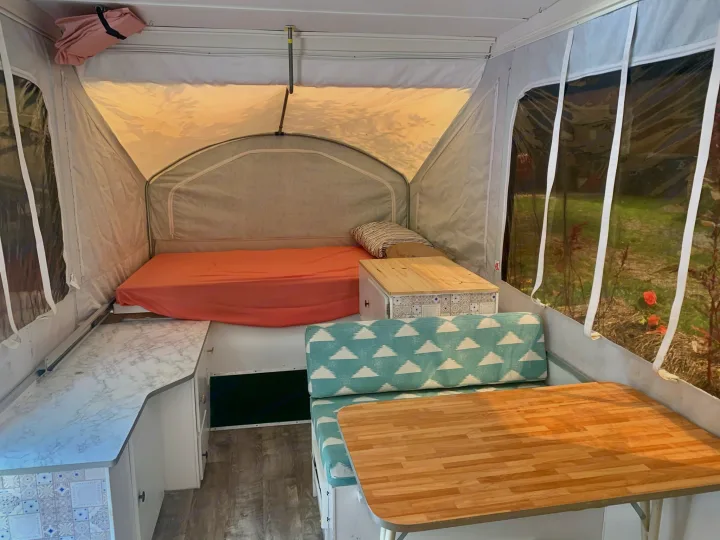 Cozy pop-up RV rental interior with bed, dinette, and kitchen counter, offering compact, functional living space.. Viking Pop Up 2004