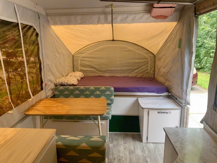 Interior of an RV rental pop-up camper featuring a cozy bed, dining area, and cabinet with a 'No Smoking' sign.. Viking Pop Up 2004