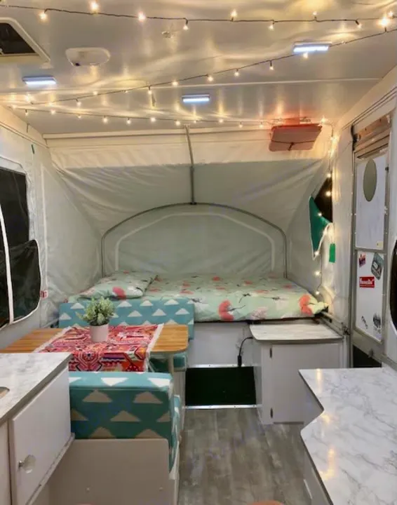 This cozy pop-up camper interior, ideal for an rv rental, features string lights, a bed, and dining space.. Viking Pop Up 2004