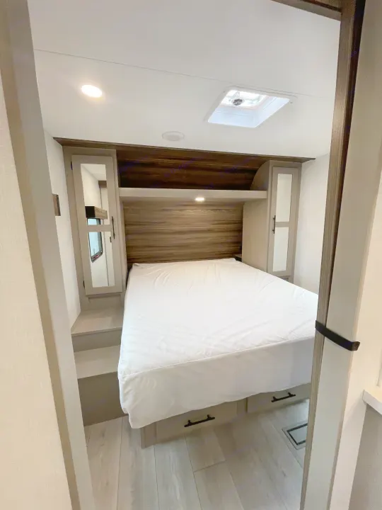 View of a modern RV rental bedroom with a neatly made bed, wooden headboard, and built-in storage on the sides and under.. KZ CONNECT 271BHSE 2026