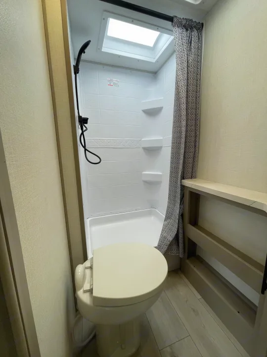 This compact RV rental bathroom features a toilet, shower with patterned curtain, ceiling skylight, and storage shelving.. KZ CONNECT 271BHSE 2026