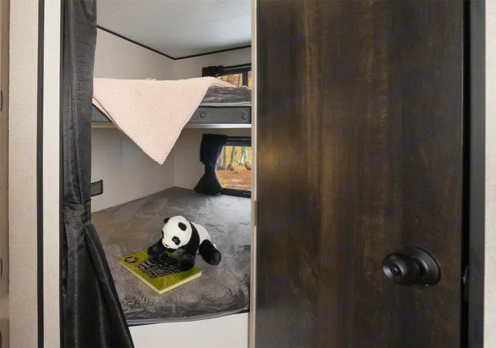 Cozy bunk beds in this RV rental. A plush panda and a book rest on the lower bunk, with a forest view outside the window.. Starcraft Autumn Ridge 2018