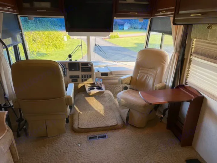 Spacious RV rental cockpit with beige captain's chairs, dashboard, front window view, and side table.. Winnebago Adventurer 2004