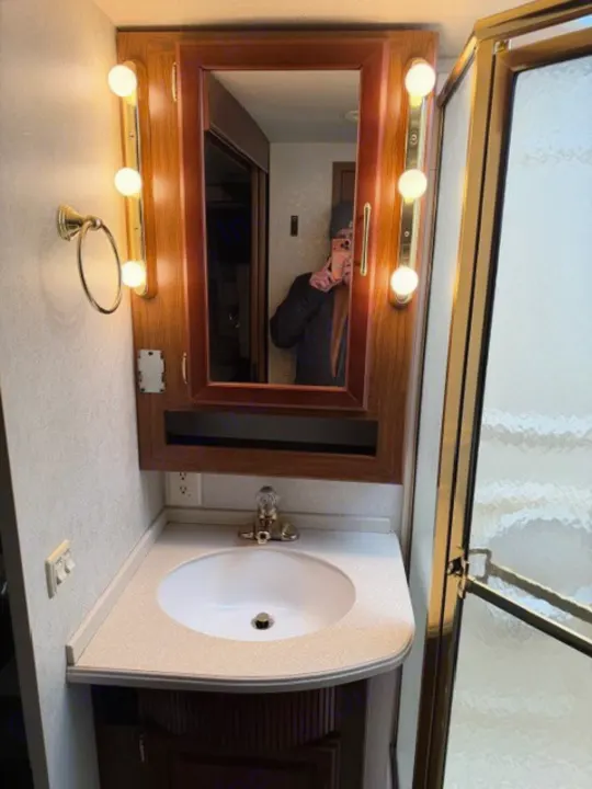 This RV rental bathroom has a sink, wood vanity, lighted mirror cabinet, and adjacent shower, offering comfort on the road.. Winnebago Adventurer 2004