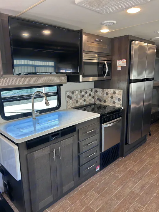 Modern RV rental kitchen space, featuring dark cabinets, stainless steel appliances, a TV, sink, and wood-look flooring.. Forest River Georgetown 2020