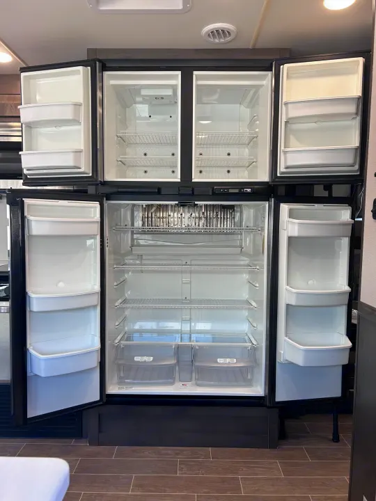 Empty, multi-door RV rental refrigerator, fully open, showing wire freezer shelves & spacious fridge crisper drawers.. Forest River Georgetown 2020