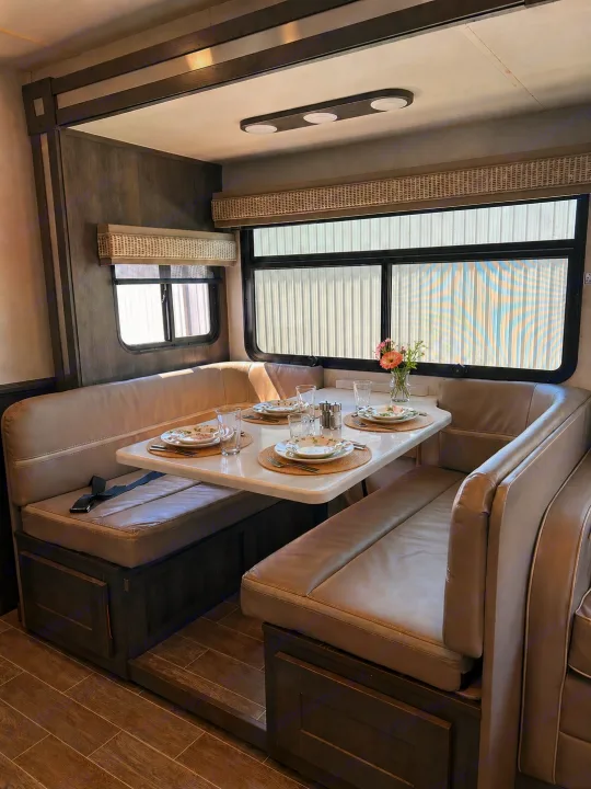 Cozy RV rental dining booth with a light-colored upholstered dinette, dark wood base, and set table, next to large windows.. Forest River Georgetown 2020