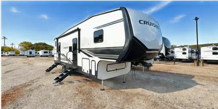 White and black fifth-wheel RV rental parked on a gravel lot with steps extended, under a clear sky. Ready for adventure.. Cruiser RV 32BH 2025
