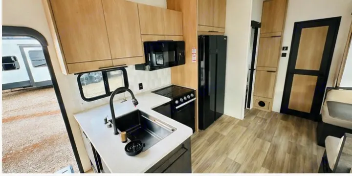 Modern RV rental kitchen features sleek black appliances, light wood cabinets, white counters, and a large sink.. Cruiser RV 32BH 2025