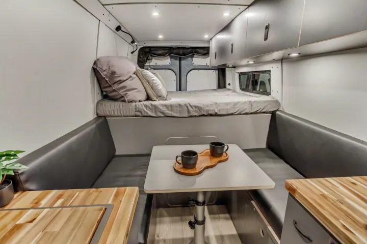 Modern rv rental interior with a comfy raised bed, dining table, and sleek overhead storage for adventurers.. Mercedes-Benz Sprinter 2025