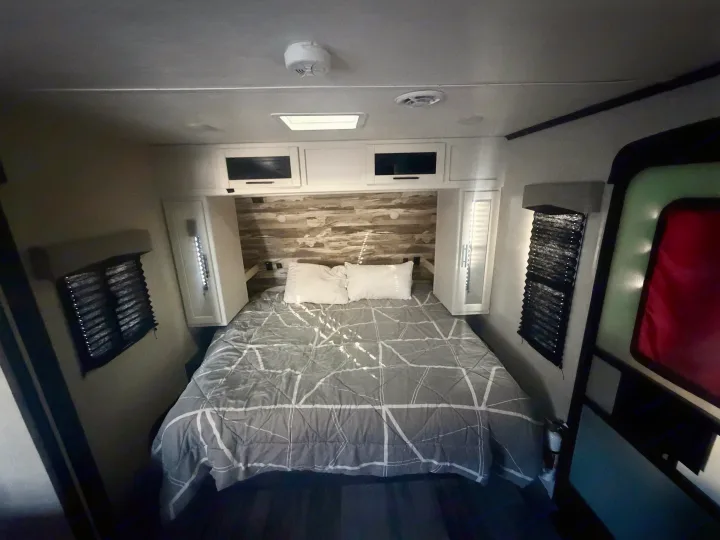 This RV rental bedroom features a comfy queen bed, rustic wood accent wall, overhead cabinets, and blinds.. Crossroads RV Cruiser Aire 2022