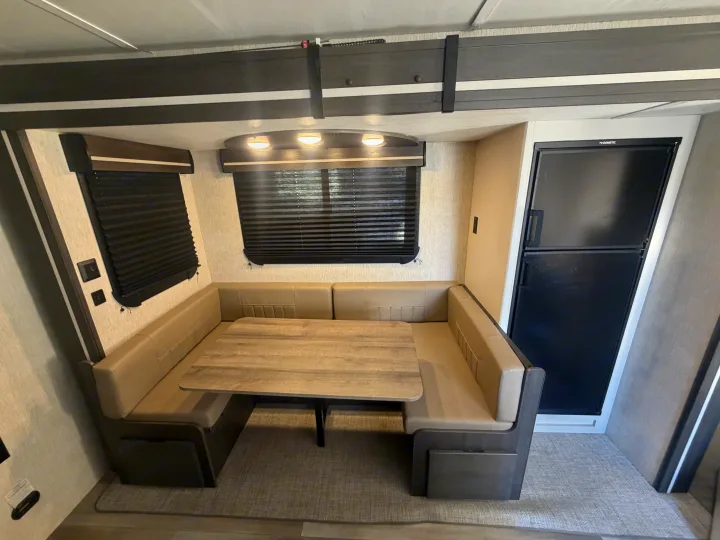 This rv rental shows a comfortable dinette area with a table, U-shaped benches, windows with blinds, and a refrigerator.. Crossroads RV Cruiser Aire 2022