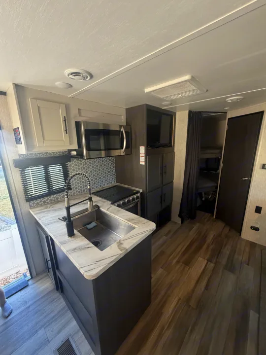 Spacious rv rental kitchen with modern amenities: sink, stove, microwave, & bunk beds. Light wood-look floors & marble counters.. Crossroads RV Cruiser Aire 2022