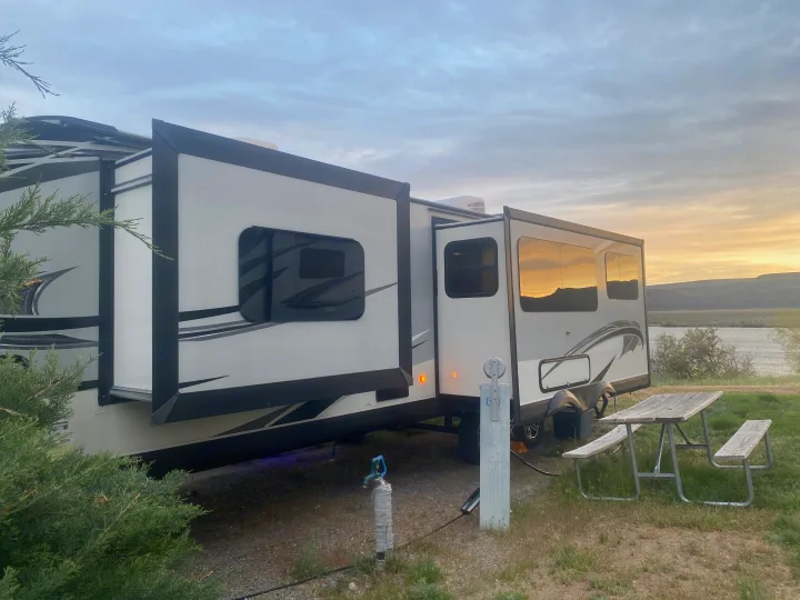 Waterside RV rental showing extended slide-outs, hookups, and a picnic table at sunset, ready for camping.. Jayco White Hawk 2020