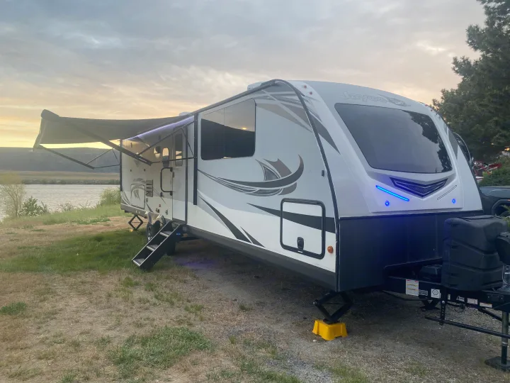Waterfront Jayco RV rental with awning & blue accent lights at dusk, perfect for a peaceful camping trip.. Jayco White Hawk 2020