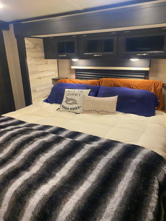 Comfortable RV rental bedroom with a plush bed, navy pillows, a striped blanket, and dark overhead storage cabinets.. Jayco White Hawk 2020