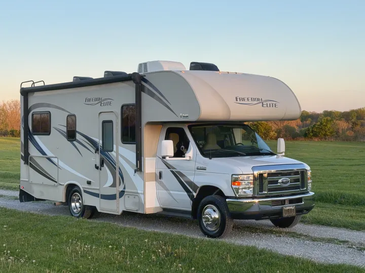White Freedom Elite Class C rv rental (Ford E-350) with a dog in the window, parked on gravel. Your next travel adventure awaits!. Thor Freedom Elite 2017