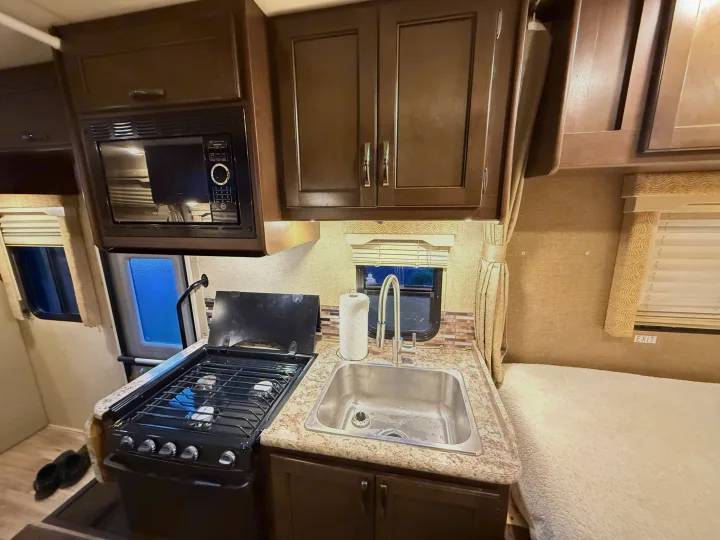 RV rental kitchen space with microwave, gas stove, sink, and wood cabinets. Compact and ready for adventure.. Thor Freedom Elite 2017