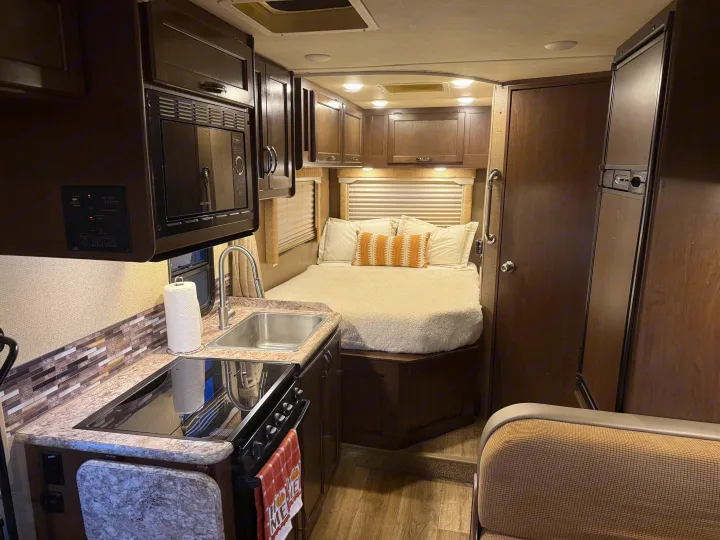 RV rental: compact kitchen (sink, stove, microwave) on left, cozy bedroom with bed on right.. Thor Freedom Elite 2017