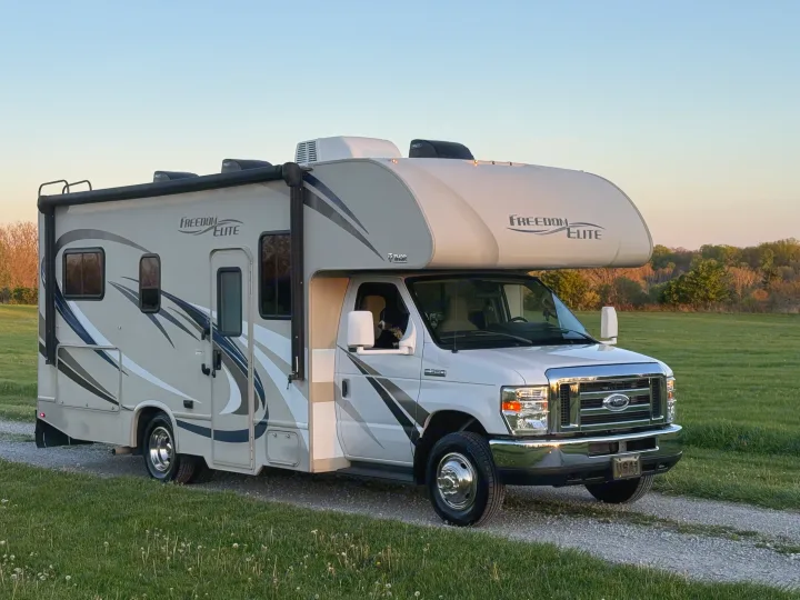 White and gray Freedom Elite Class C rv rental, built on a Ford E-350 chassis, ready for adventure on a gravel path.. Thor Freedom Elite 2017