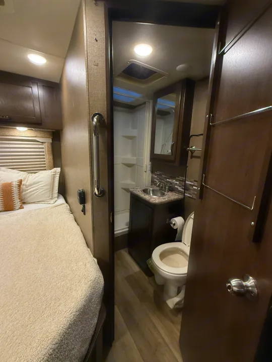 Compact rv rental interior featuring a cozy bedroom on the left and a small bathroom with toilet, sink, and shower.. Thor Freedom Elite 2017